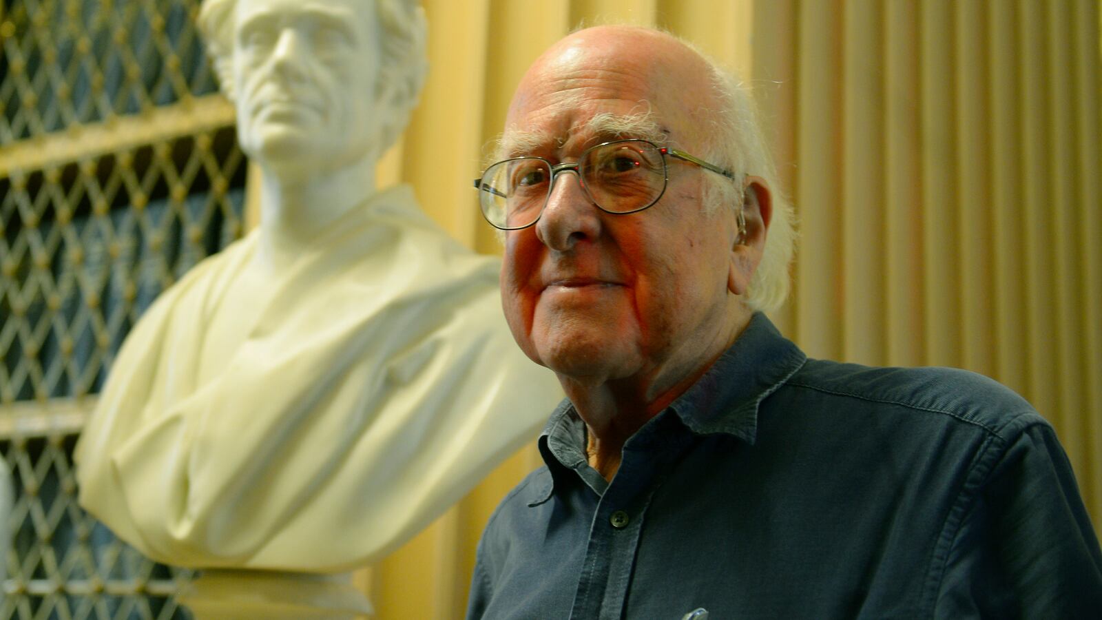 Peter Higgs poses for a photograph next to a statute in 2013.