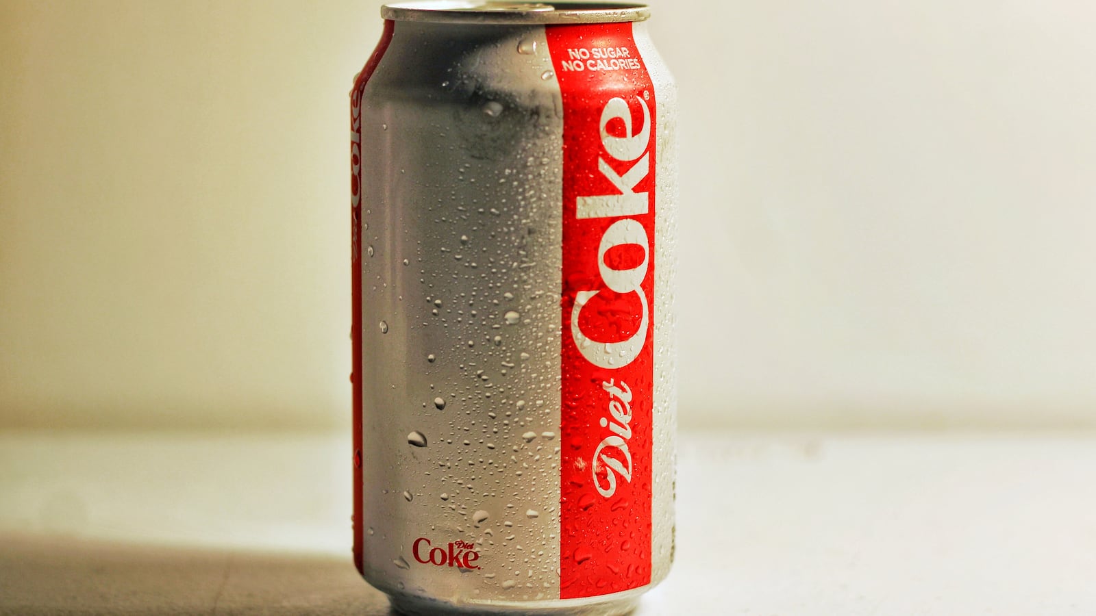 A sweating can of Diet Coke on a white surface against a white background.