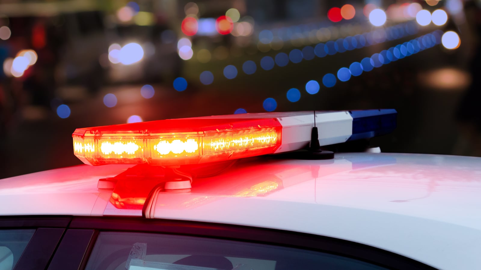 Red flashing sirens on top of police car against blurred urban background. Close-up