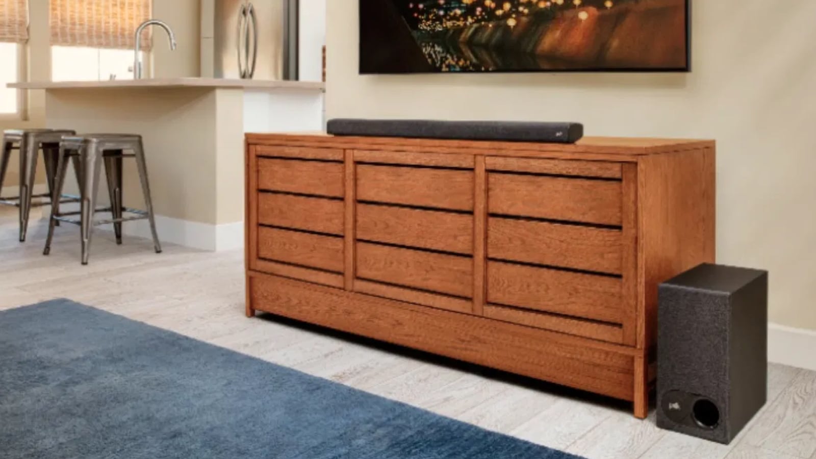 A living room TV setup. There is a flatscreen TV on the wall, a brown stand with a sounbar on it and a subwoofer next to it.