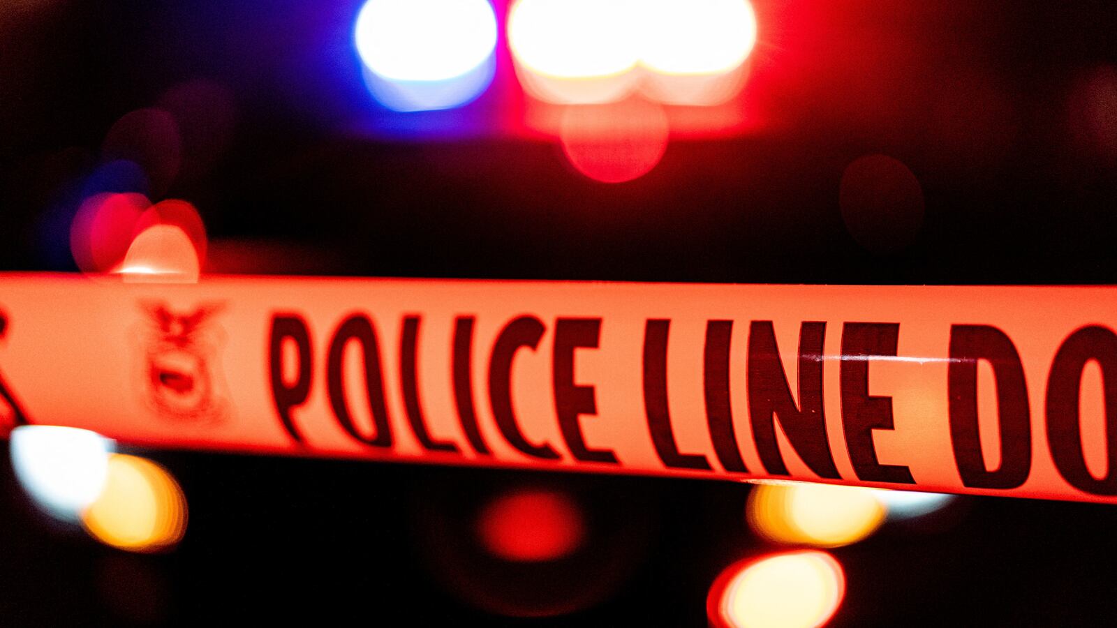 Police tape in front of flashing police lights.