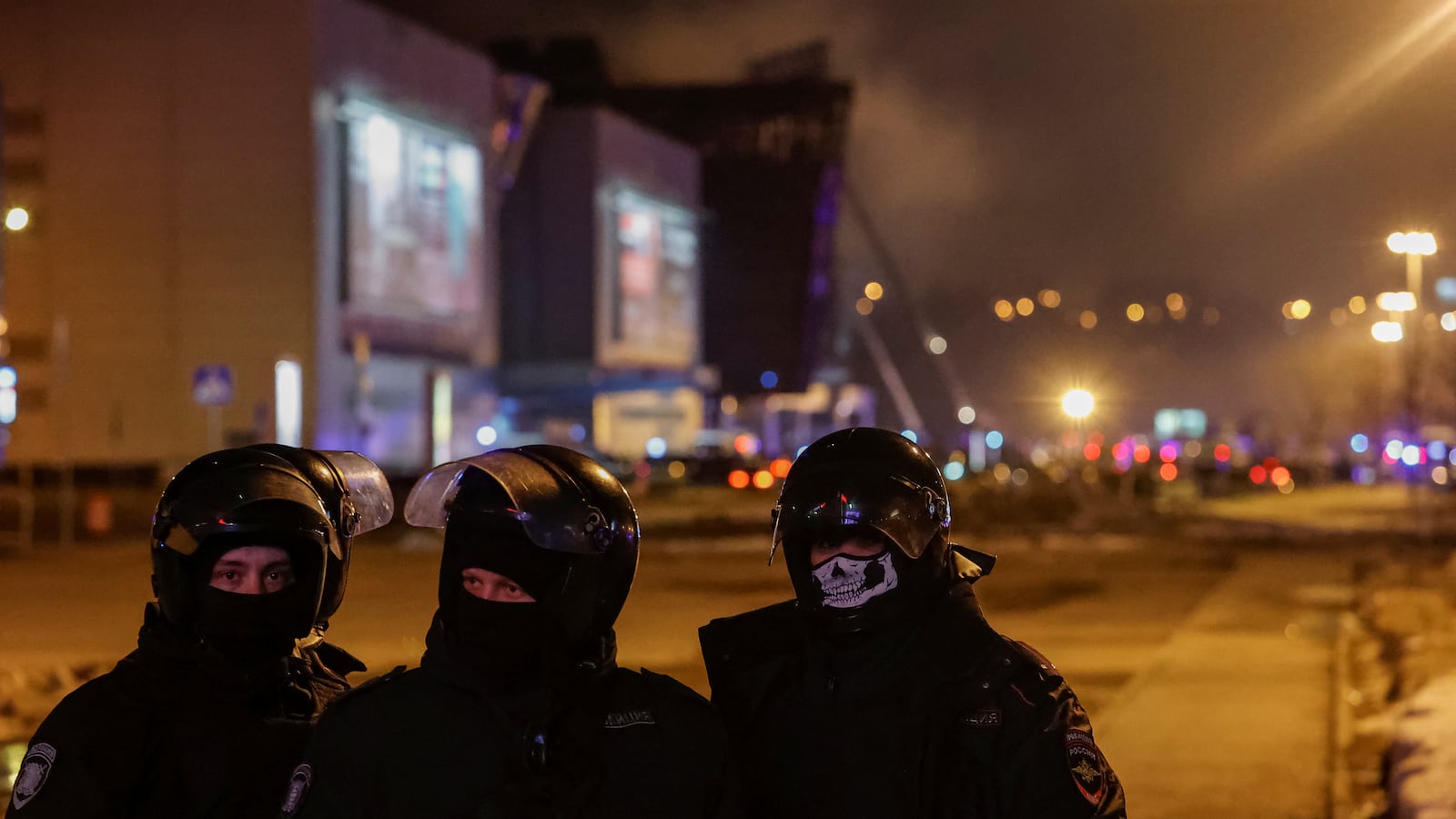 Law enforcement officers in masks stand guard near the burning Crocus City Hall venue
