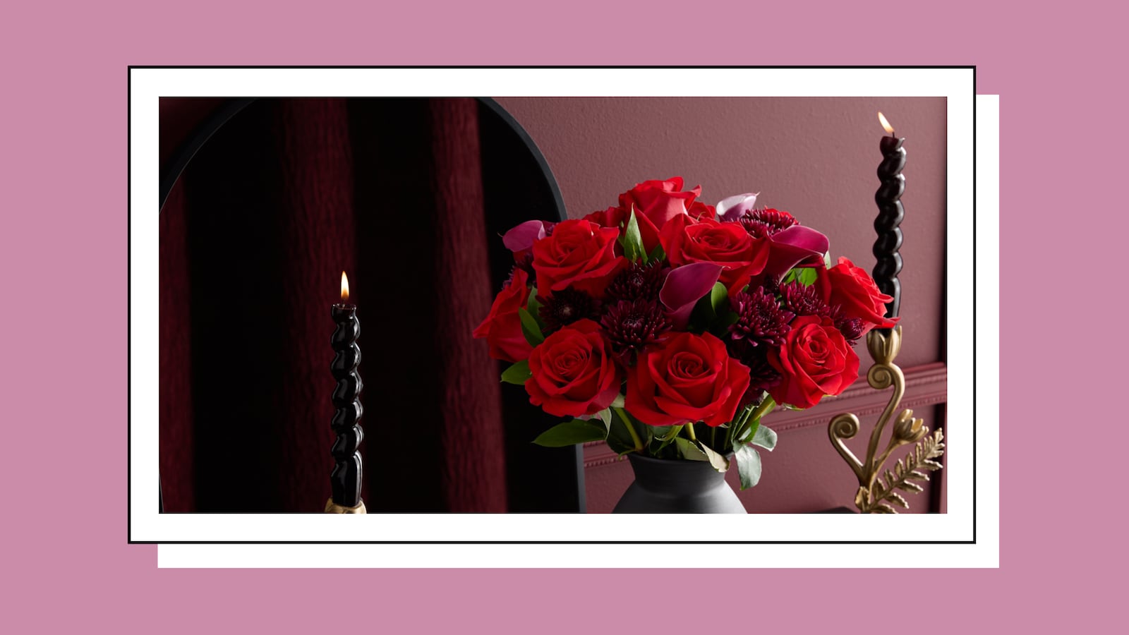 Romantic Valentine’s Day floral arrangement from 1-800-Flowers featuring red roses in a modern vase, styled with black taper candles for an elegant at-home setting.