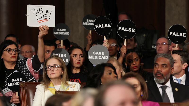Democrats hold protest signs as Trump speaks.