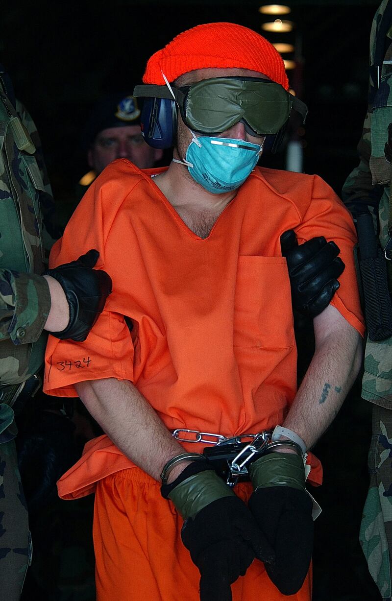 A man in orange jump suit bound and blindfolded with ear protecters