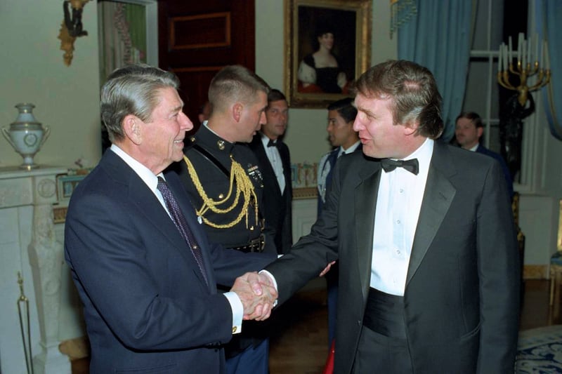 Ronald Reagan in blue suit shaking hands with Donald Trump in tuxedo, with a military assistant to Reagan's right