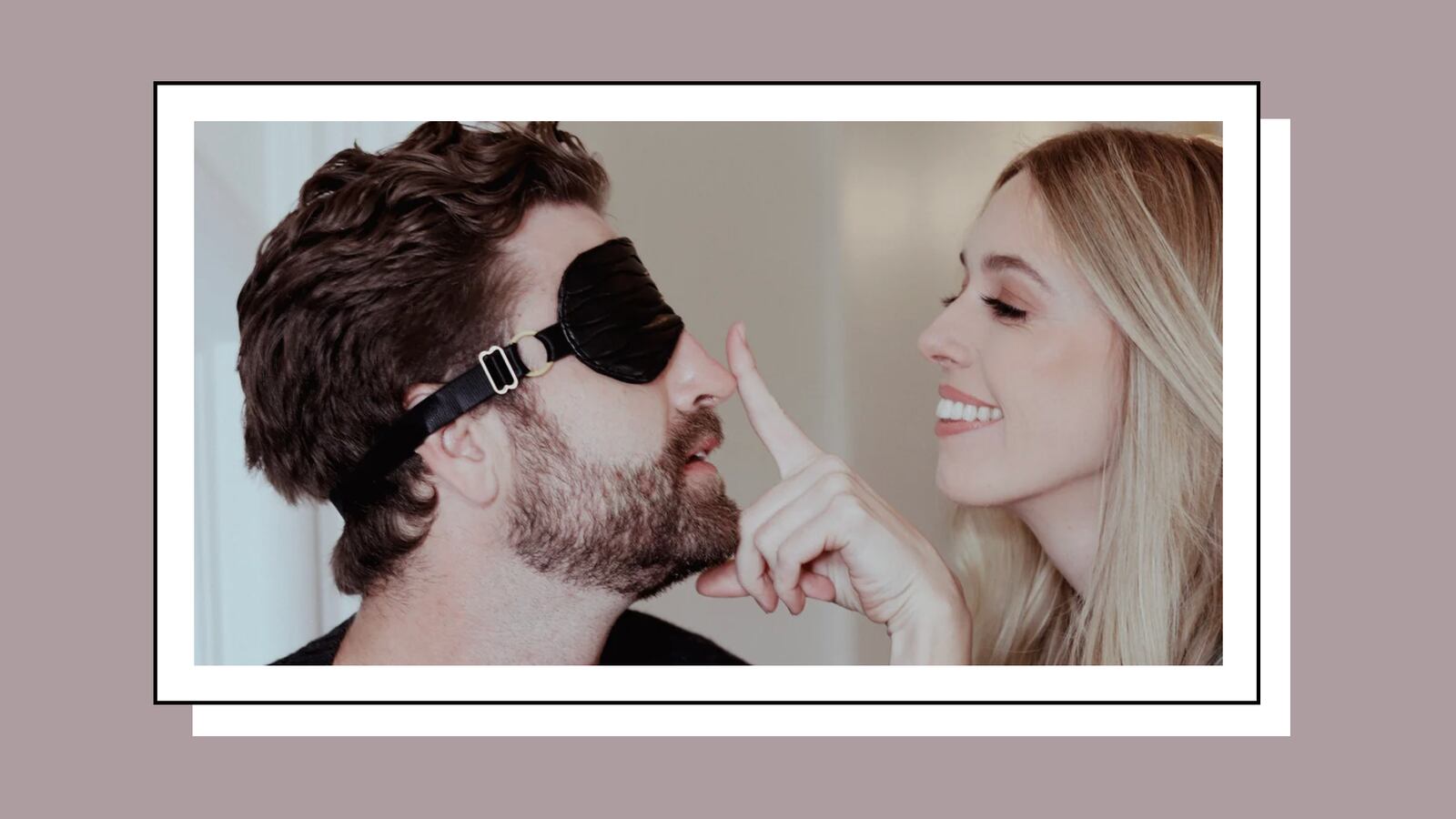 A couple enjoying a playful moment, with the man wearing a black blindfold and the woman smiling while gently touching his nose.