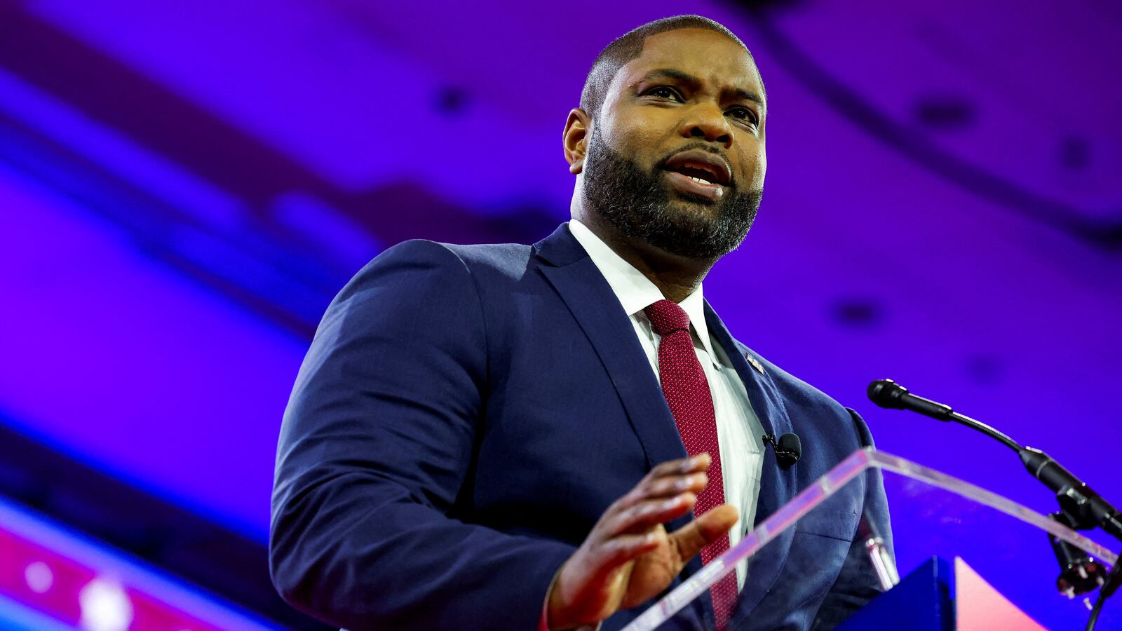 Byron Donalds speaks on stage at CPAC, wearing a suit and tie.