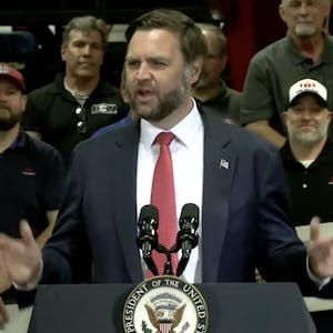 Vice President JD Vance speaking at a manufacturing plant in Missouri standing in front of around a dozen men holding placards that read: "Made in America"