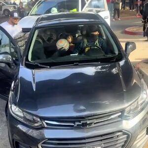 With one masked officer in the driver's seat, another in the passenger seat throws a beachball into the face of the child sitting in the back seat.