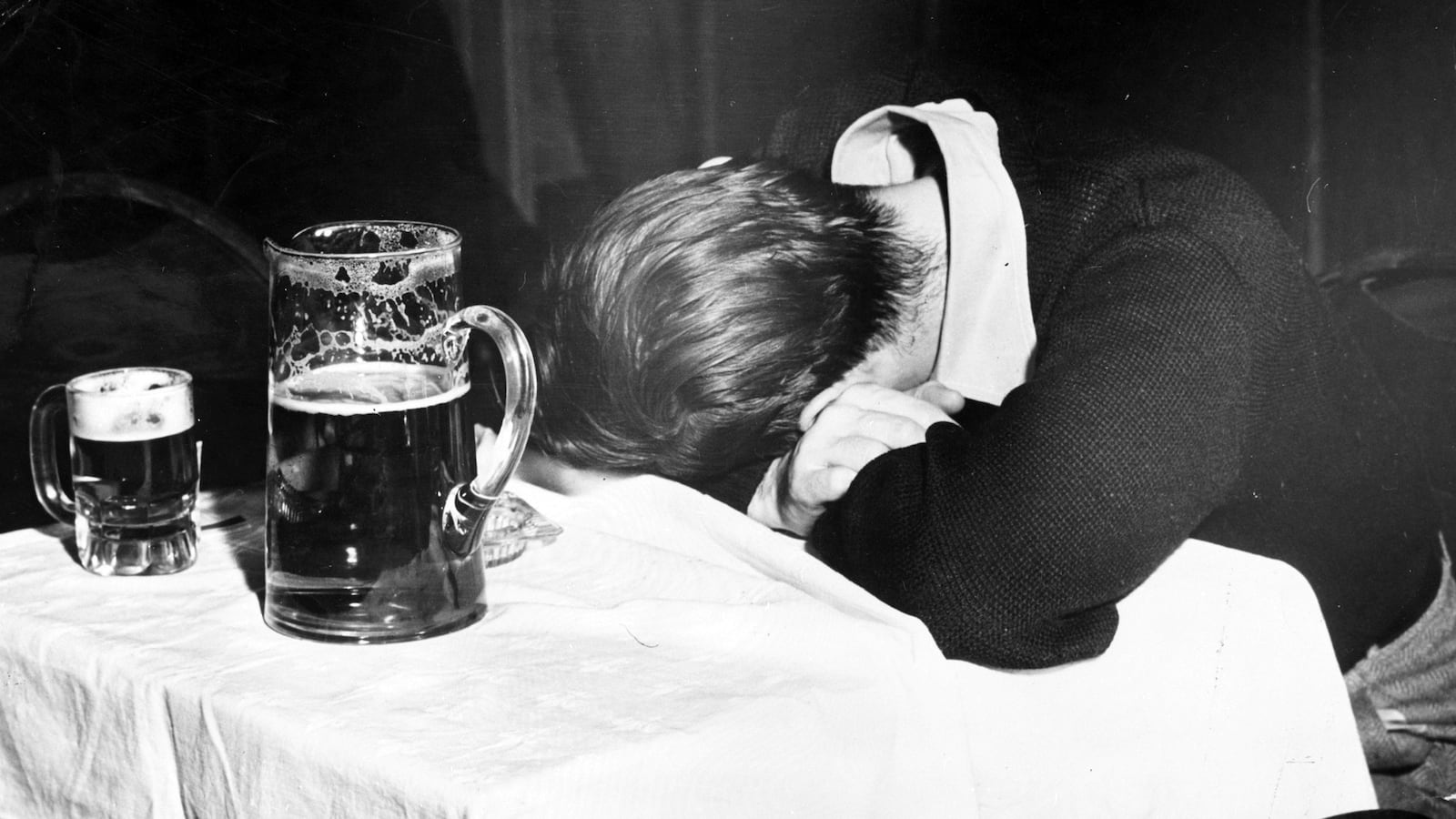 A man sleeps with his head on a table beside a pitcher of beer and a half-empty glass in a New York City bar.