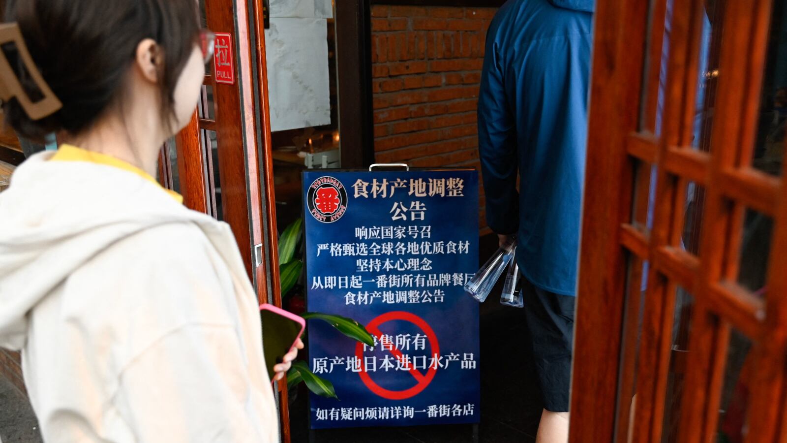 People walk into an area of Japanese restaurants past a sign reading "Suspend the sale of all fish products imported from Japan", in Beijing on August 27, 2023.