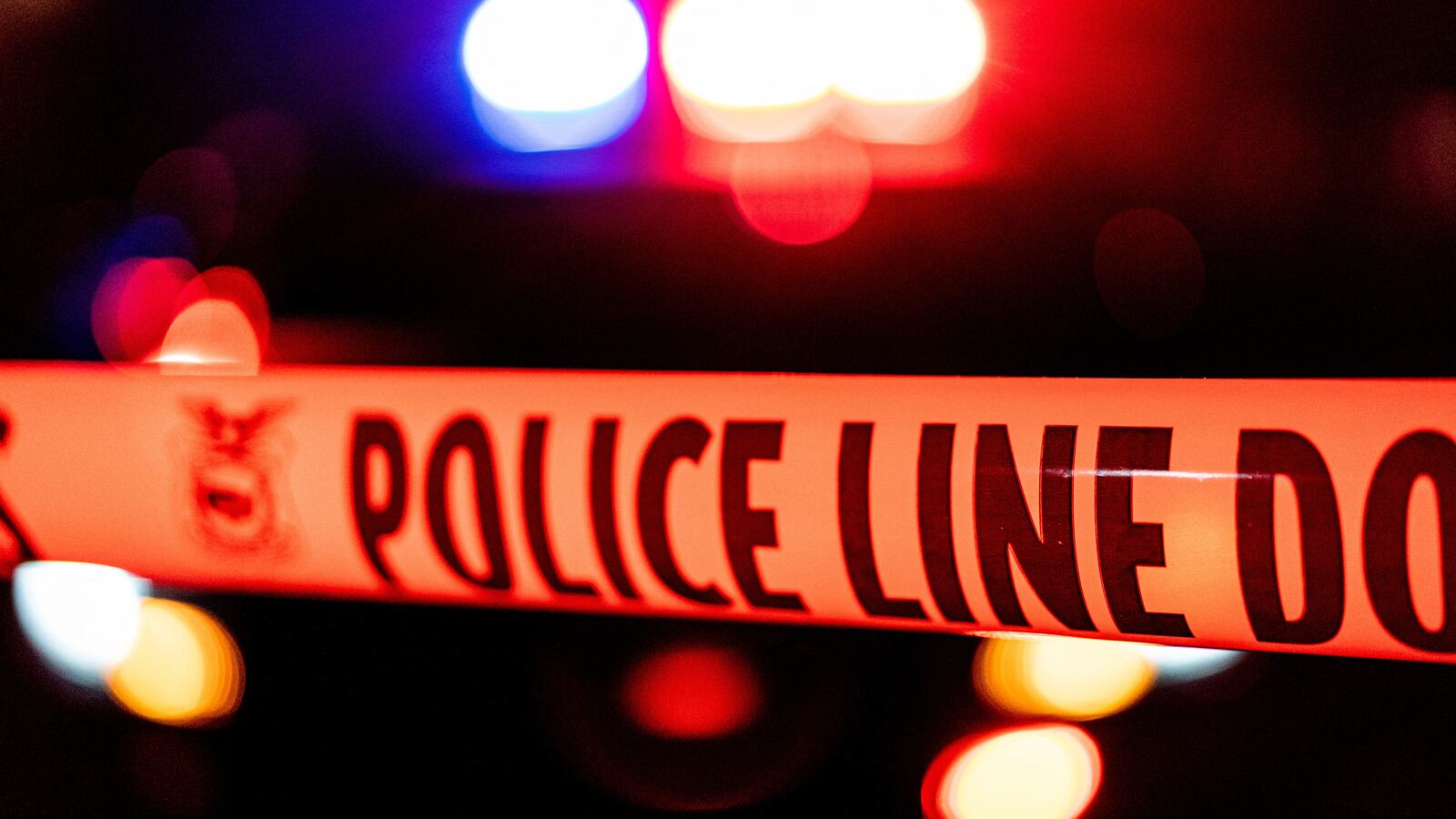 Police tape in front of flashing police lights.