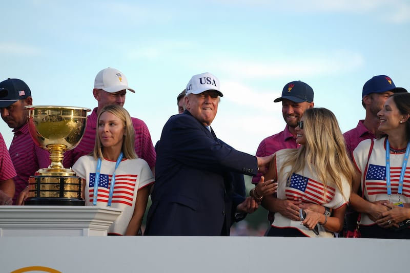 President Donald Trump pats Wyndham Clark's girlfriend Emily Tanner on the shoulder as he joins members of the U.S. Team during the trophy ceremony at the Presidents Cup golf tournament at Medinah Country Club in Medinah, Illinois, US, September 27, 2026.