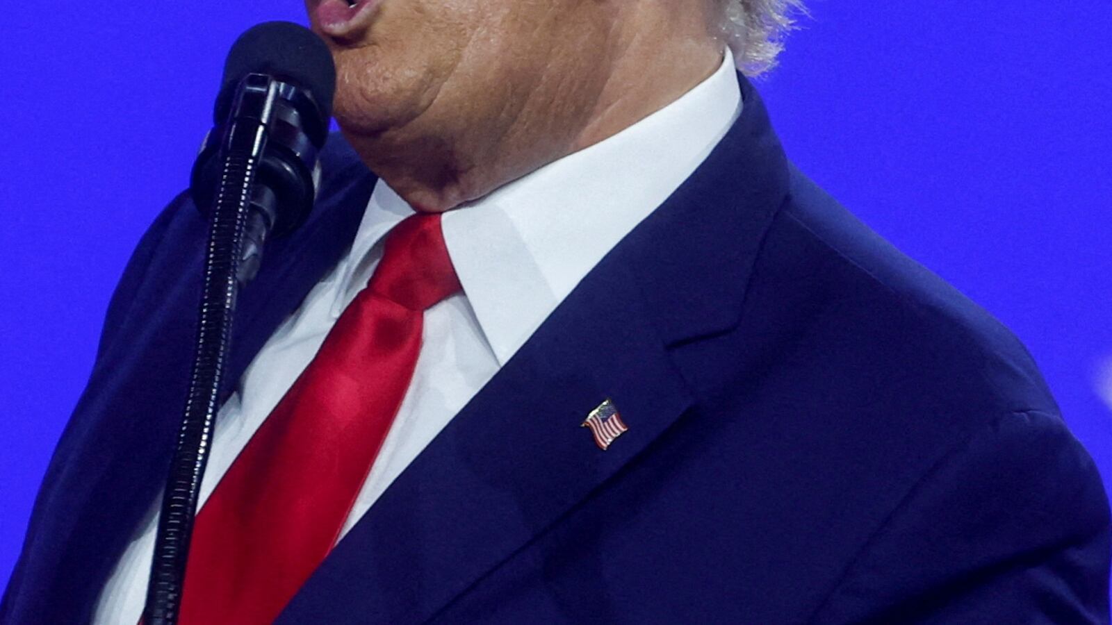 Donald Trump speaks into a microphone in front of a blue screen