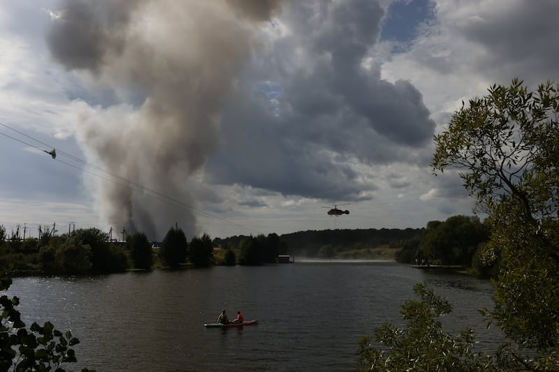 MOSCOW, RUSSIA - AUGUST 16: People spend time near the river as a firefighting helicopter collects water to extinguish the fire that broke out in a distribution warehouse near Moscow, Russia after Ukraine's drone attack on August 16, 2026. (Photo by Stringer/Anadolu via Getty Images)
