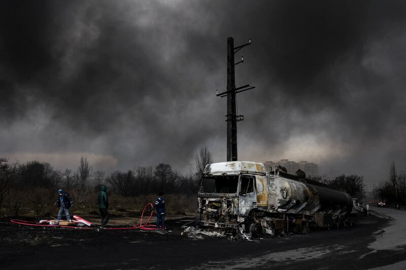 People stand near a destroyed vehicle as smoke rises after a reported strike on Shahran fuel tanks, amid the U.S.-Israeli conflict with Iran, in Tehran, Iran, March 8, 2026. Majid Asgaripour/WANA (West Asia News Agency) via REUTERS ATTENTION EDITORS - THIS PICTURE WAS PROVIDED BY A THIRD PARTY     TPX IMAGES OF THE DAY