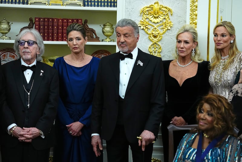 Sylvester Stallone (C) looks on during a medal presentation ceremony with U.S. President Donald Trump for the 2025 Kennedy Center Honorees in the Oval Office of the White House on December 06, 2025 in Washington, DC. Notice the use of the cane.