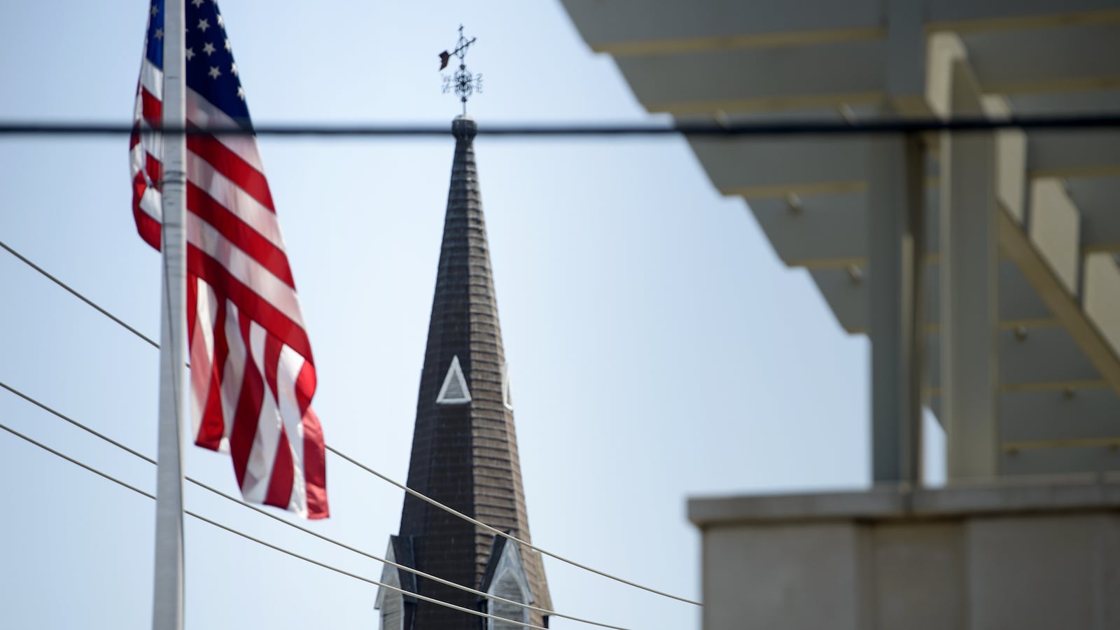 An American Flag flies in front of a church steeple.