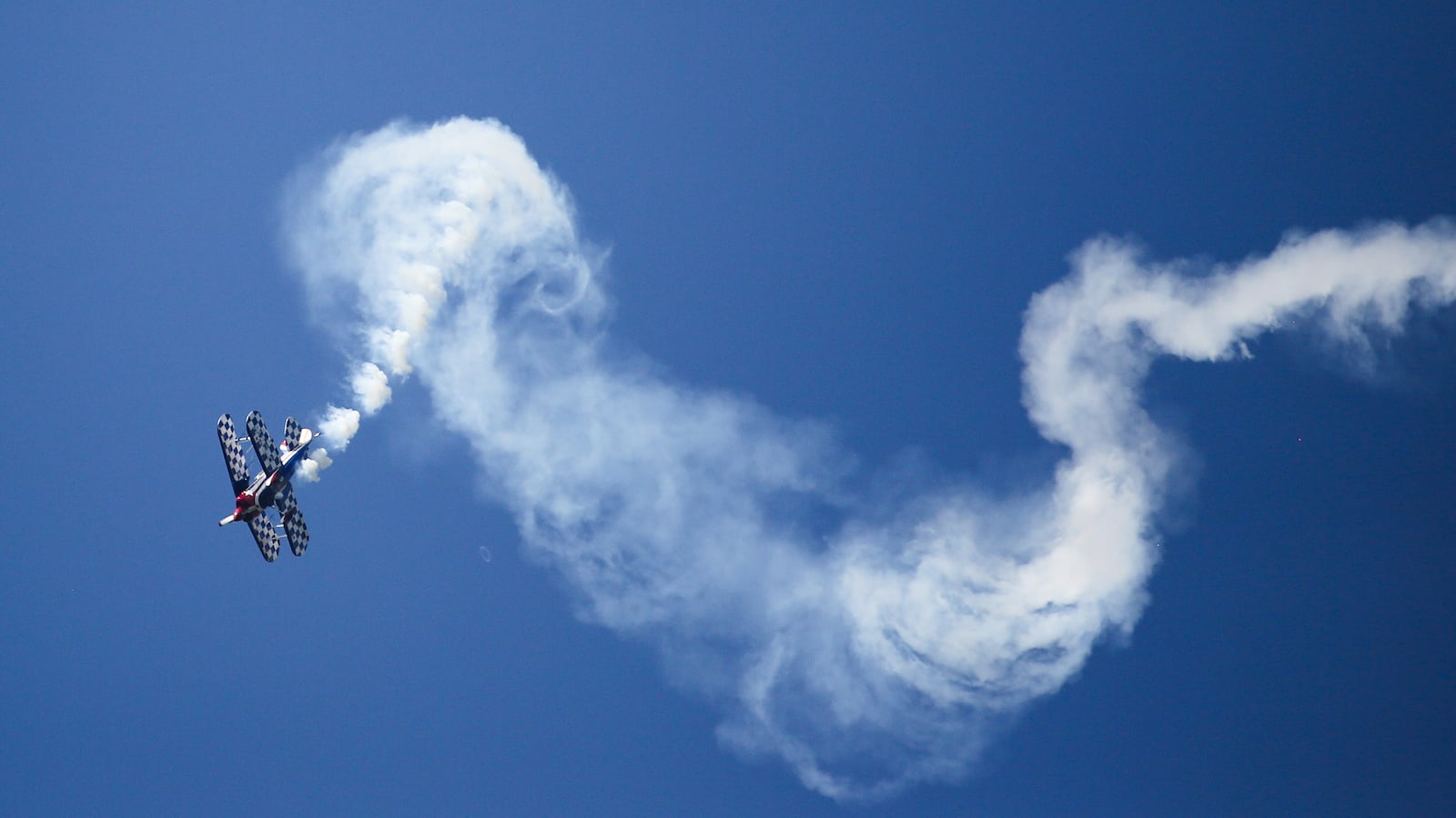 A Pitts S1S biplane aerobatic plane flies on the Swabian Alb, trailing white clouds of fog