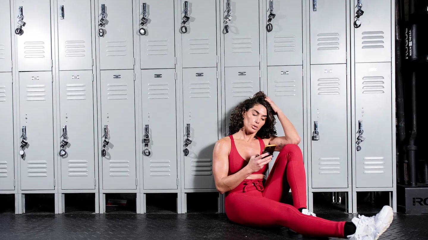 Woman in locker room wearing fitness gear and looking at the Caliber app