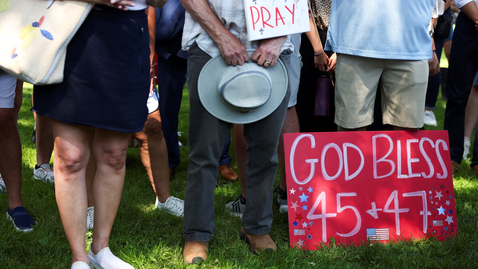People stand next to sign that reads, “God bless 45 and 47.”