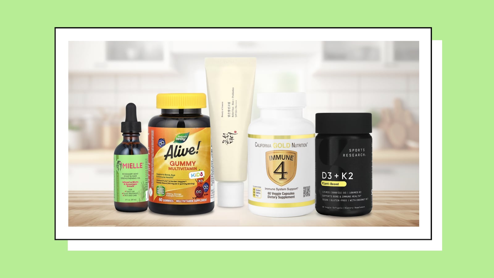 Assortment of health and wellness supplements, featuring Mielle Rosemary Mint Strengthening Oil, Alive! Kids Gummy Multivitamin, Sioris Enriched by Nature Cream, California Gold Nutrition Immune 4, and Sports Research D3 + K2 Plant-Based capsules, arranged on a wooden surface with a blurred kitchen background.