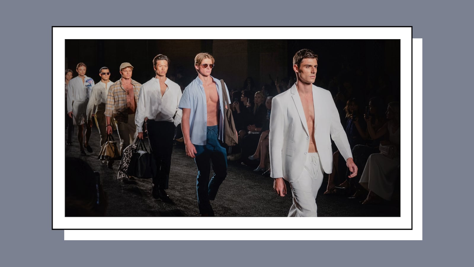 Male models walking down a fashion runway wearing stylish summer outfits including white suits, open shirts, and casual accessories at a high-fashion event.