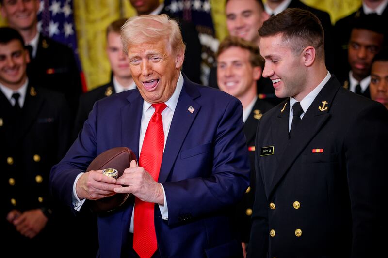 U.S. President Donald Trump reacts after Navy Midshipmen co-captain Linebacker Colin Ramos (R) presents him with a large ring during a presentation ceremony for the Commander-in-Chief Trophy to the Navy Midshipmen football team in the East Room of the White House April 15, 2025 in Washington, DC.