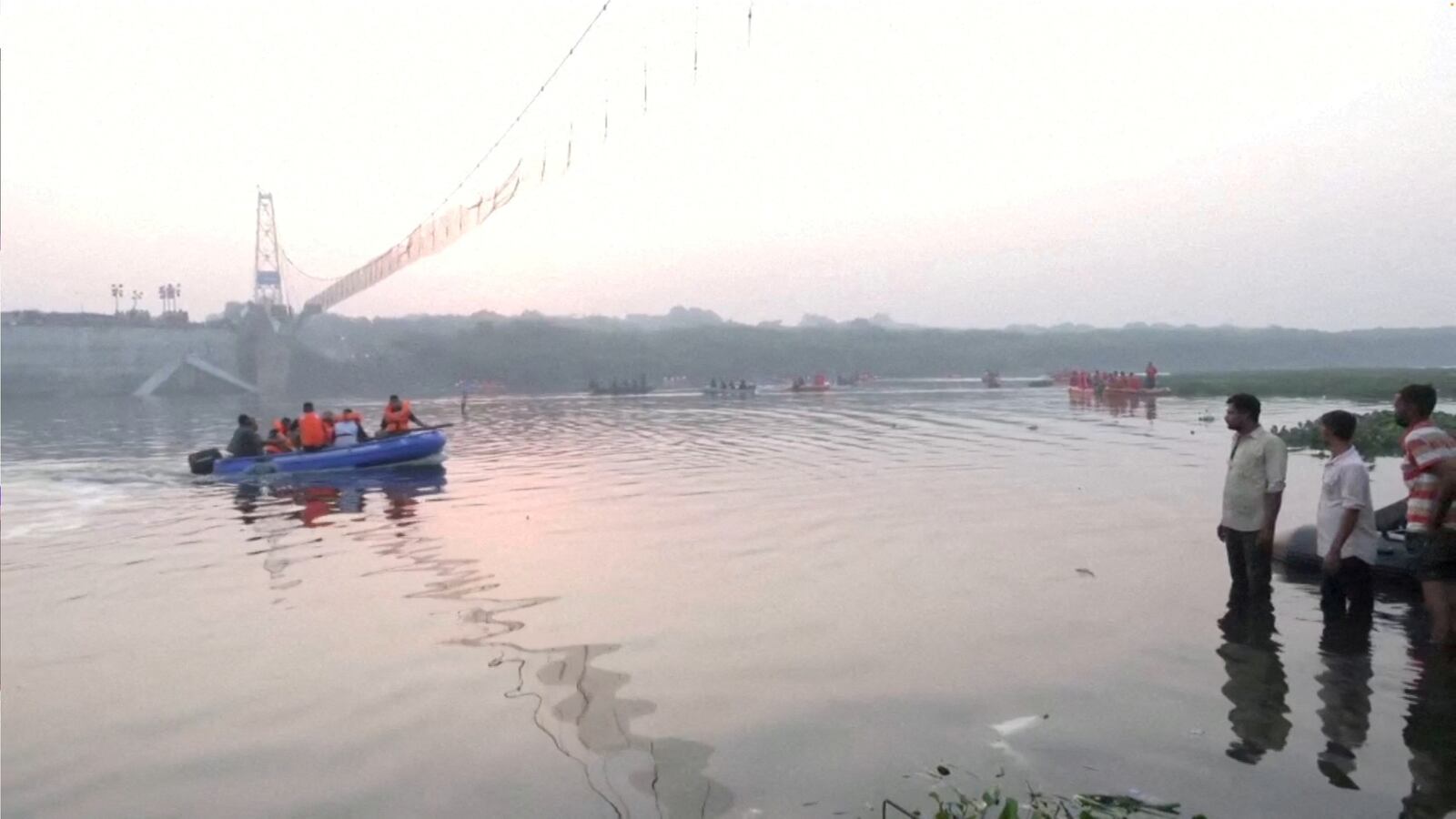 People look on as rescuers in boats work at the site of a suspension bridge collapse in Morbi town in the western state of Gujarat, India.