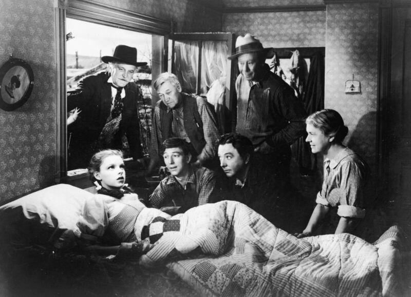 American actor and singer Judy Garland (1922 - 1969) sits up in bed while (left to right; top to bottom) Frank Morgan (1890 - 1949), Charles Grapewin (1869 - 1956), Ray Bolger (1904 - 1987), Jack Haley (1898 - 1979), Bert Lahr (1895 - 1967) and Clara Blandick (1881 - 1962) surround her in a scene from the film 'The Wizard of Oz,' 1939.