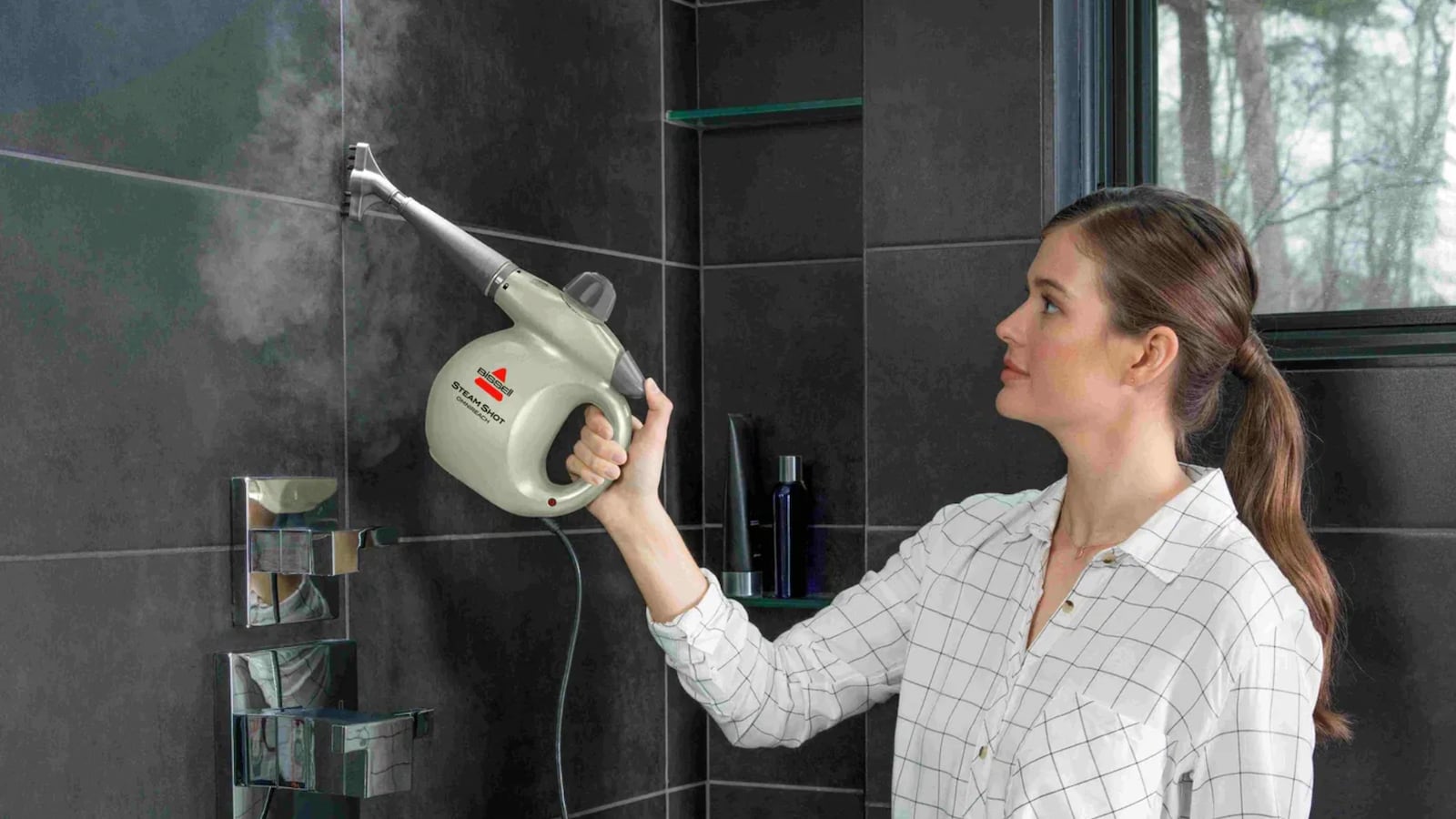 Woman using the BISSELL Steam Shot OmniReach handheld steam cleaner to clean bathroom tiles, showcasing its powerful steam cleaning capabilities.