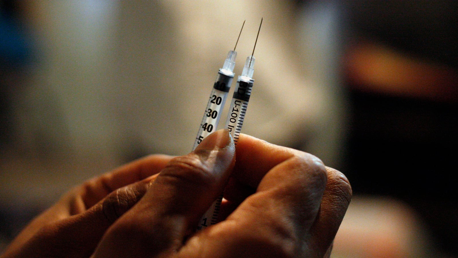 Two syringes are held by a medical professional.