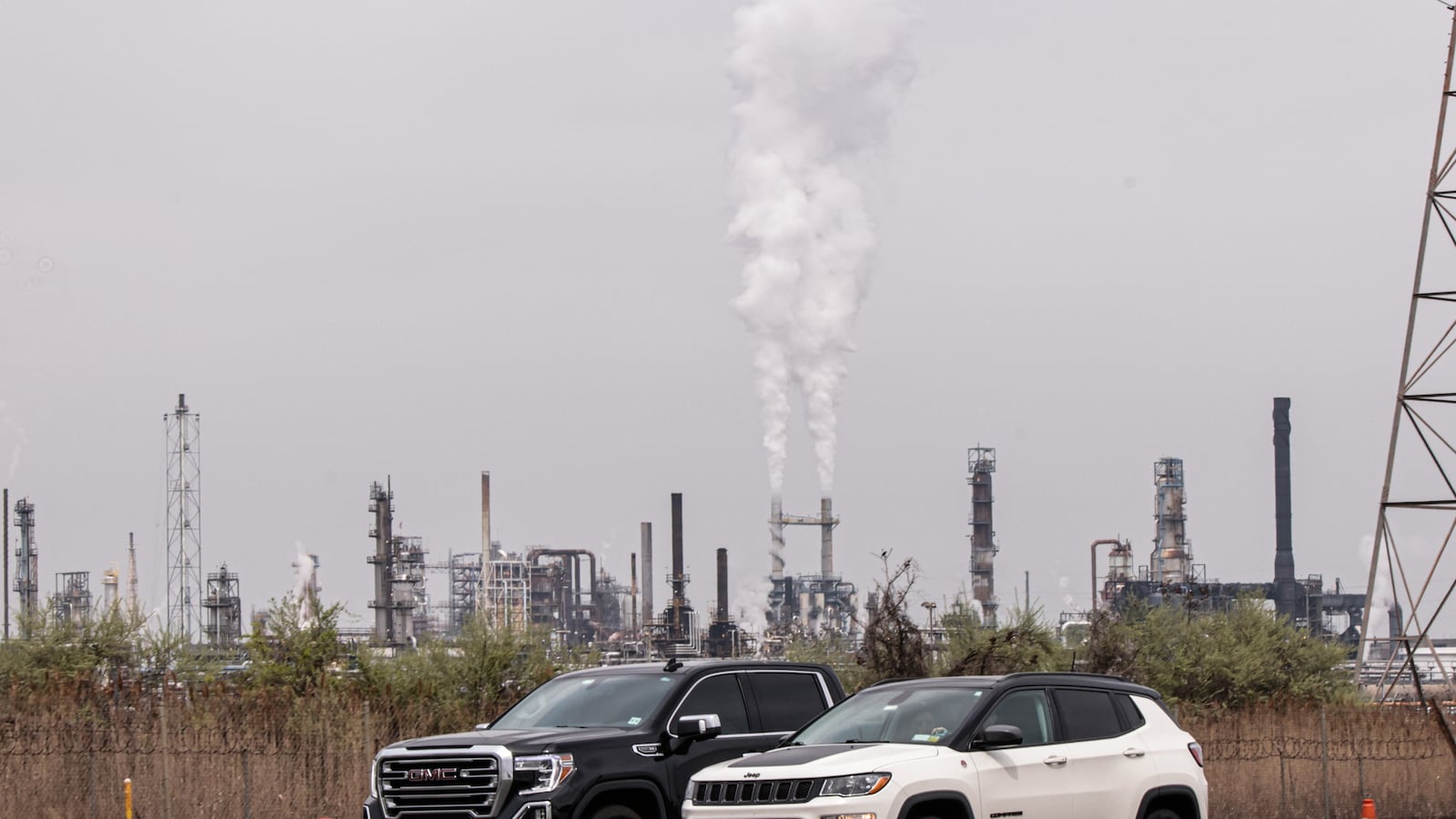 A photo of greenhouse gases being emitted from a pair of tall smokestacks in an industrial area.