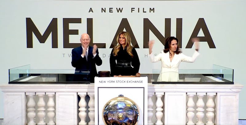 A woman gesticulates while standing beside Melania Trump in front of a sign saying "Melania: A New Film."