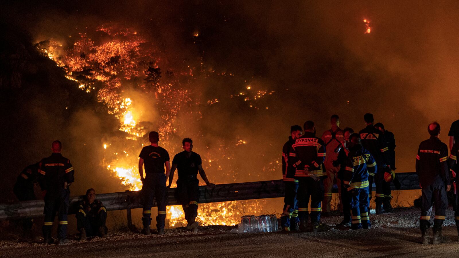Firefighters look at a wildfire burning. Greek fire department officials arrested two men for arson on Saturday as authorities attempt to tame deadly blazes in what is now the largest wildfire the European Union has ever faced.