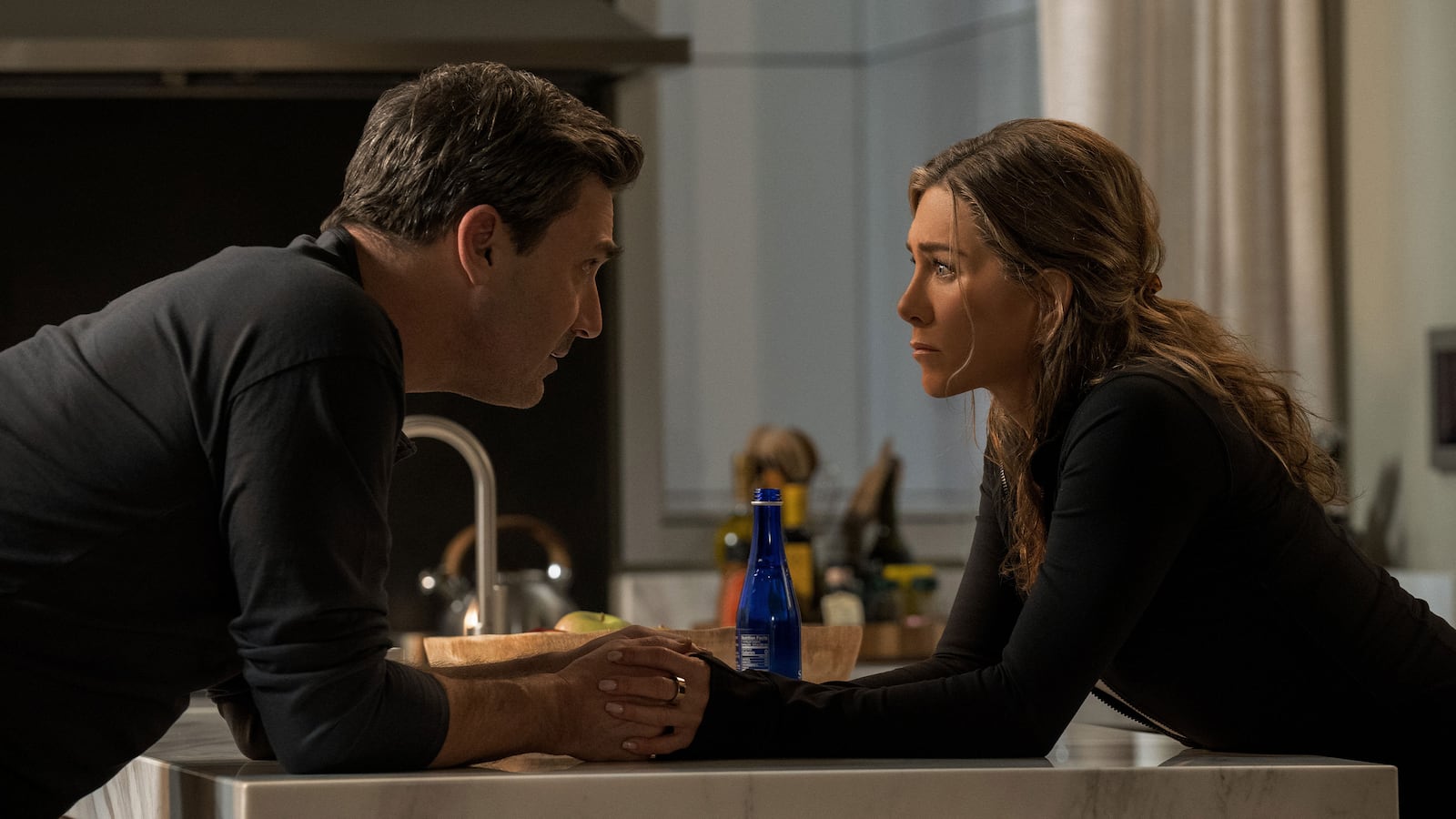 Jon Hamm holds Jennifer Aniston's hands across a desk in a still form 'The Morning Show'