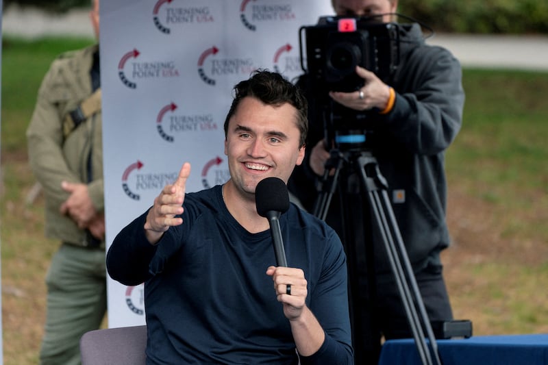 Charlie Kirk holds a debate event on a college campus, smiling and holding a microphone.
