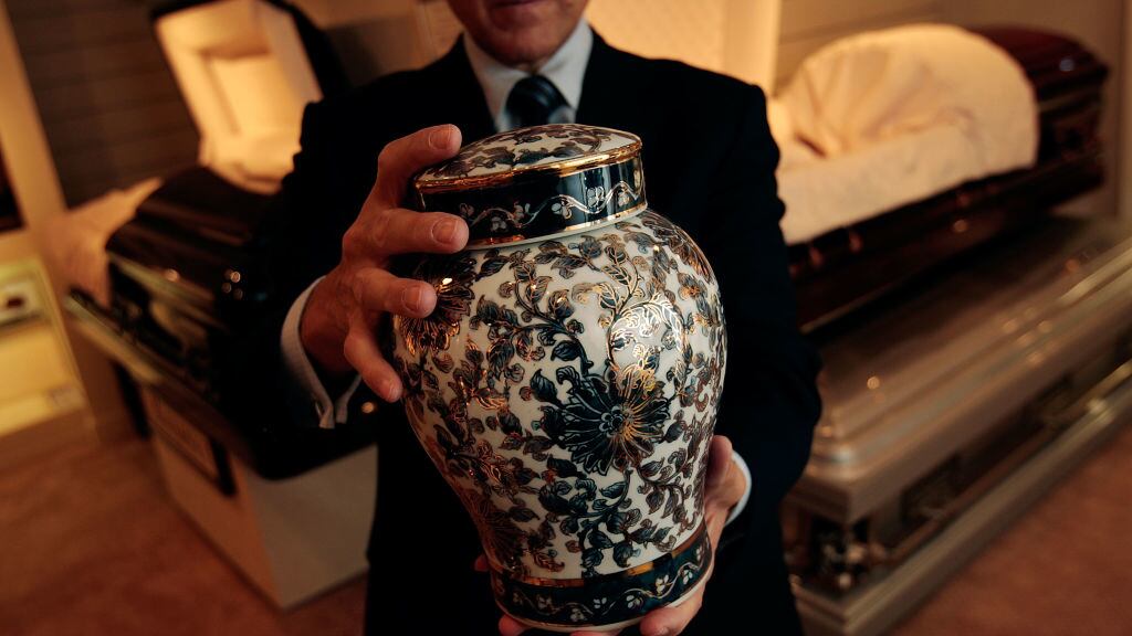 A funeral director holds an urn of ashes at a funeral parlor.