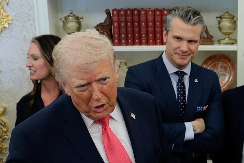U.S. President Donald Trump speaks to members of the media, with U.S. Defense Secretary Pete Hegseth standing in the background.