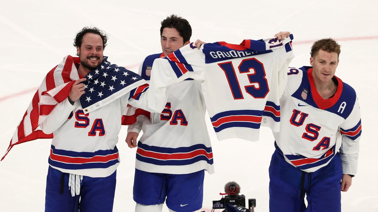 MILAN, ITALY - FEBRUARY 22: (L-R) Auston Matthews #34, Zach Werenski #8 and Matthew Tkachuk #19 of Team United States celebrate winning the gold medals with the sweater of the late Johnny Gaudreau after the team's 2-1 overtime victory in during the Men's Gold Medal match between Canada and the United States on day 16 of the Milano Cortina 2026 Winter Olympic games at Milano Santagiulia Ice Hockey Arena on February 22, 2026 in Milan, Italy.