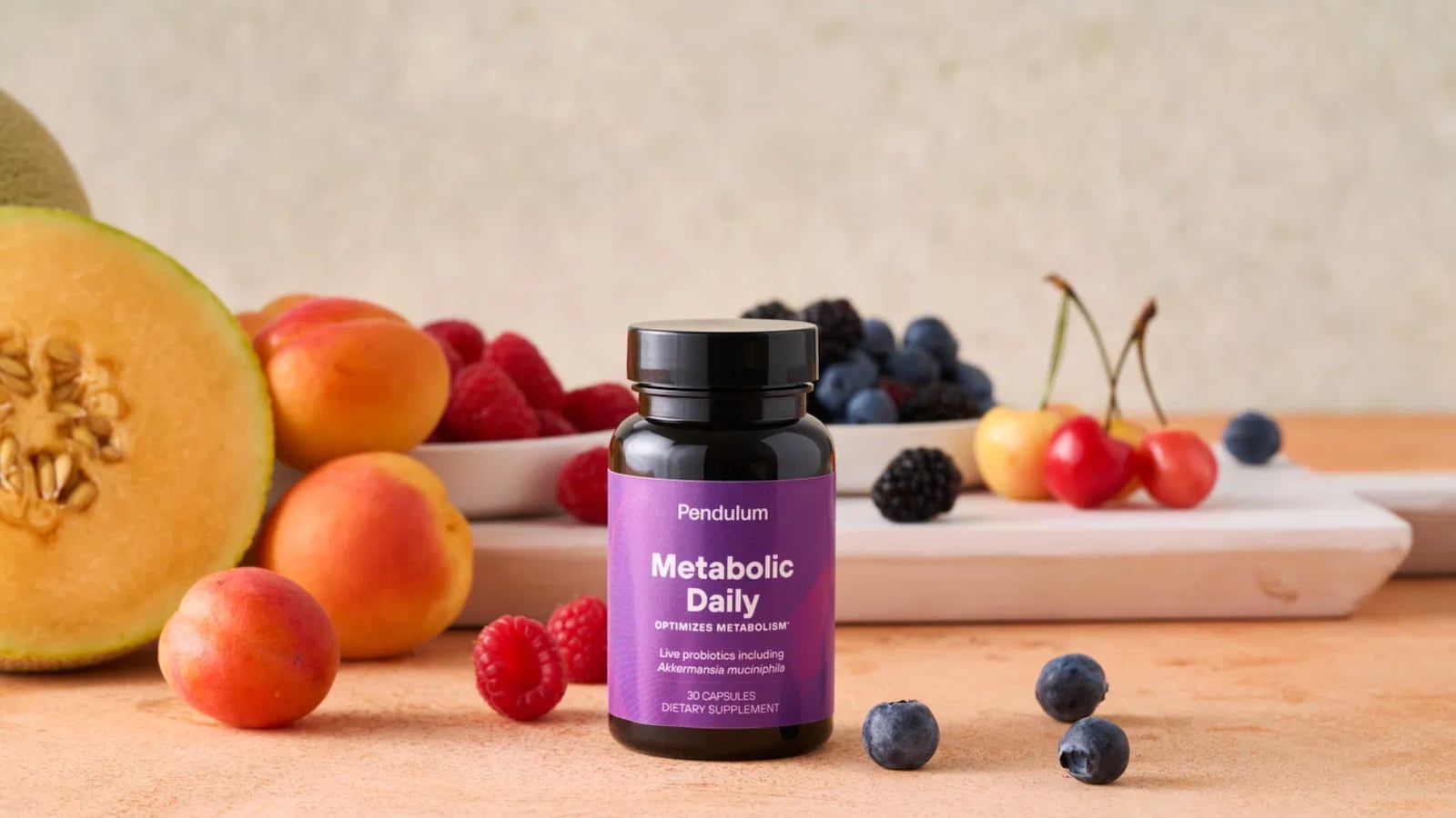 A bottle of Pendulum Metabolic Daily on a counter surrounded by fruits like blue berries, strawberries, and cherries.