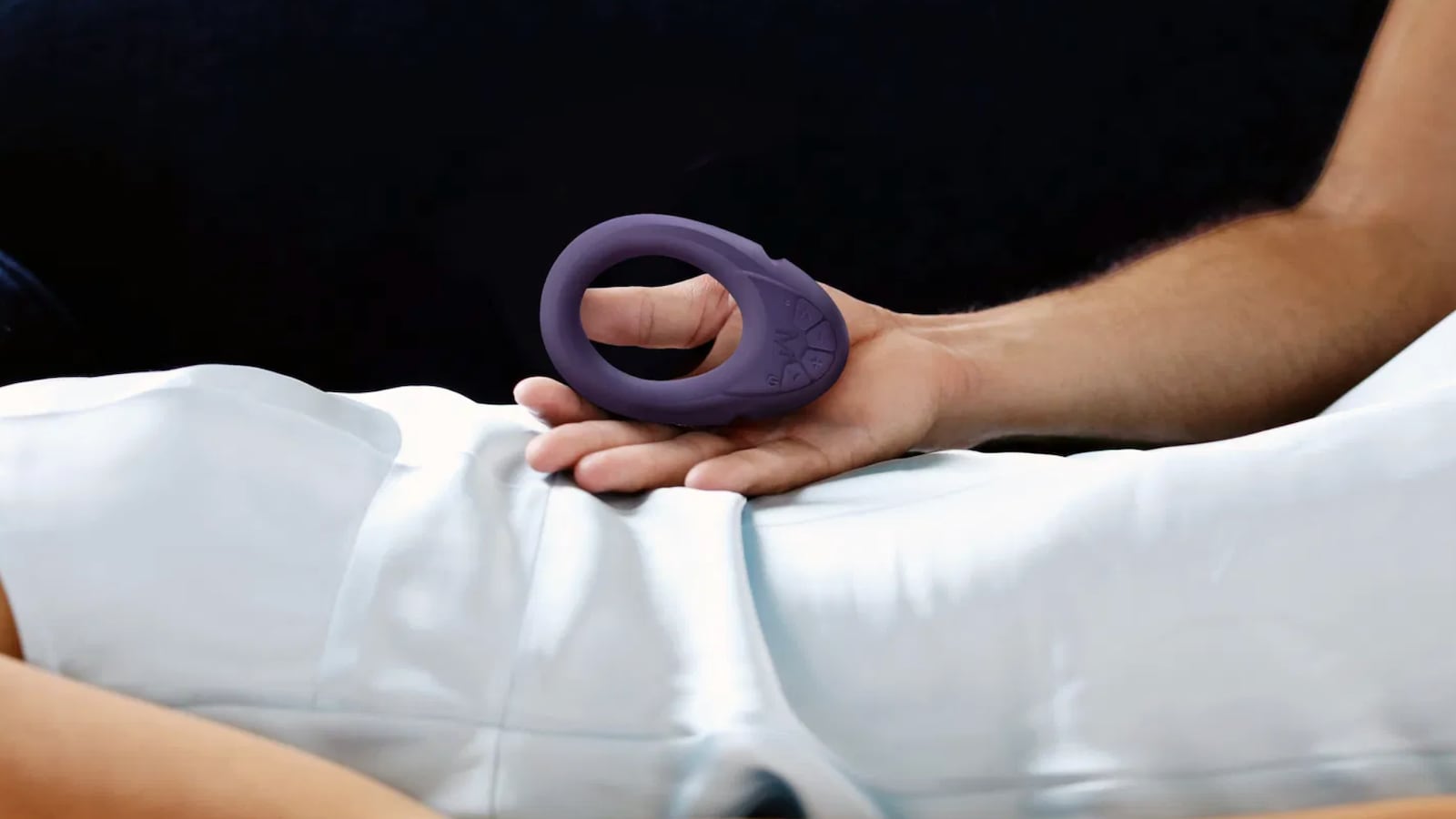 Person holding a purple MysteryVibe vibrating ring on a bed, highlighting its flexible and ergonomic design for couples' intimacy.