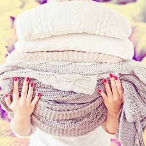 A photo illustration of a woman holding a pile of wool blankets in front of a background of sheep.