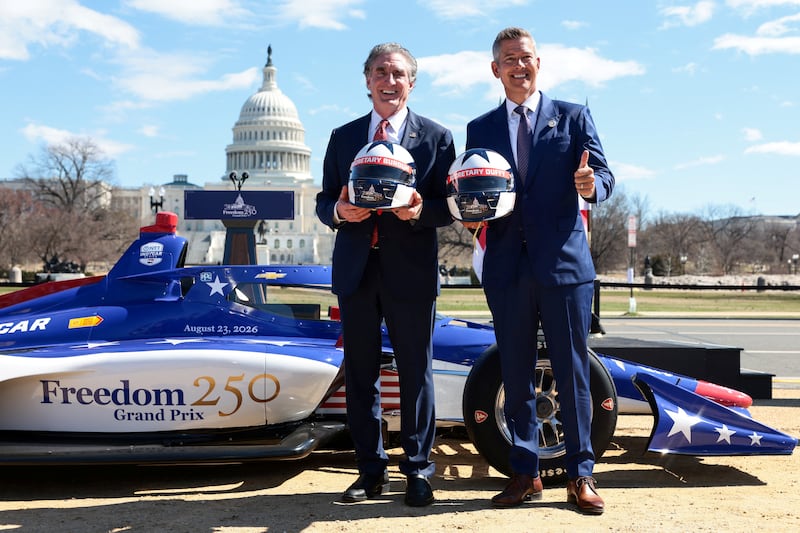 Doug Burgum and Sean Duffy pose with personalized helmets in front of Freedom250 Grand Prix racecar.