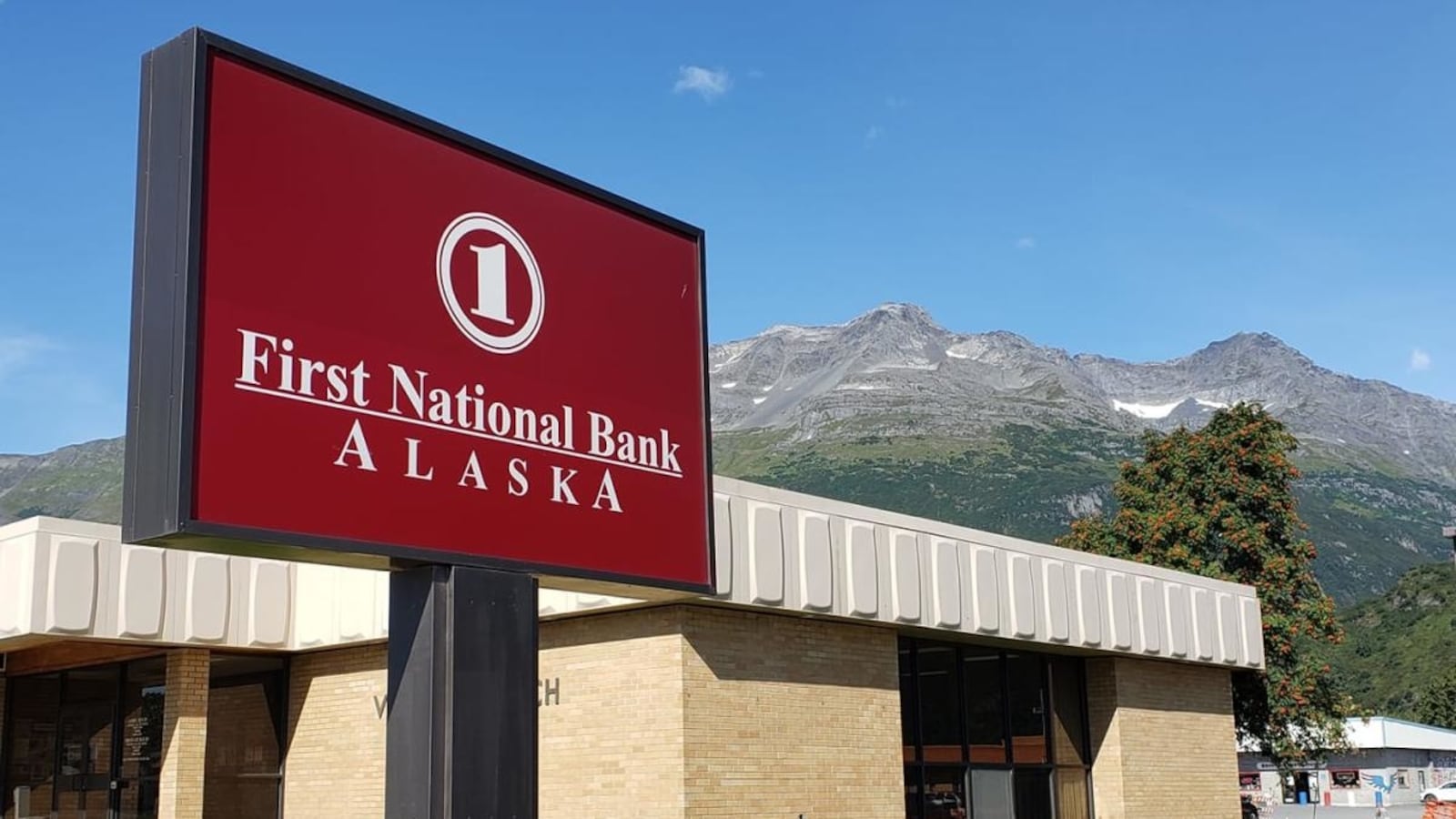 A photo of a First National Bank Alaska branch, with mountains in the distance.