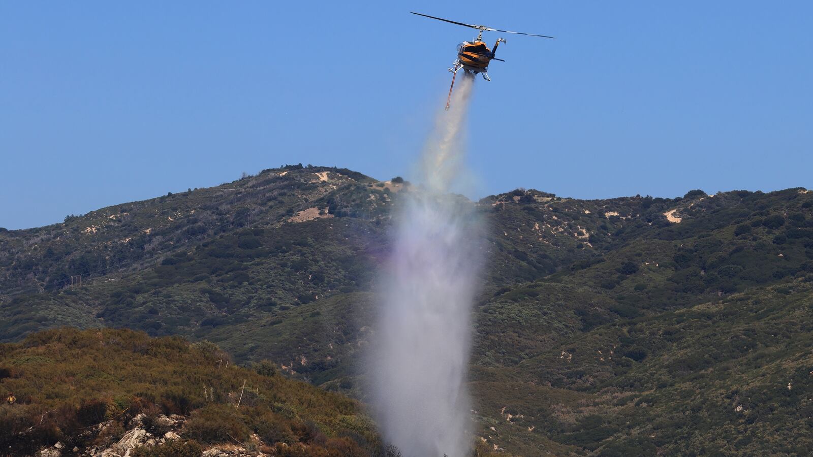 A helicopter drops water to extinguish a rapidly-growing brush fire in southern California.