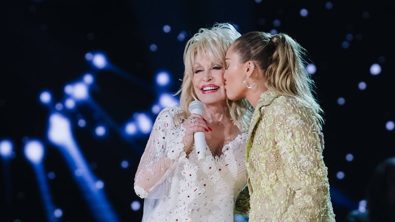Miley Cyrus is kissing Dolly Parton's cheek onstage.