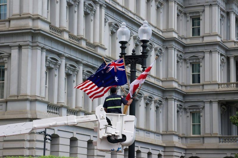 A man stands in a crane to pull down the Australian flag from a lightest outside a federal building.