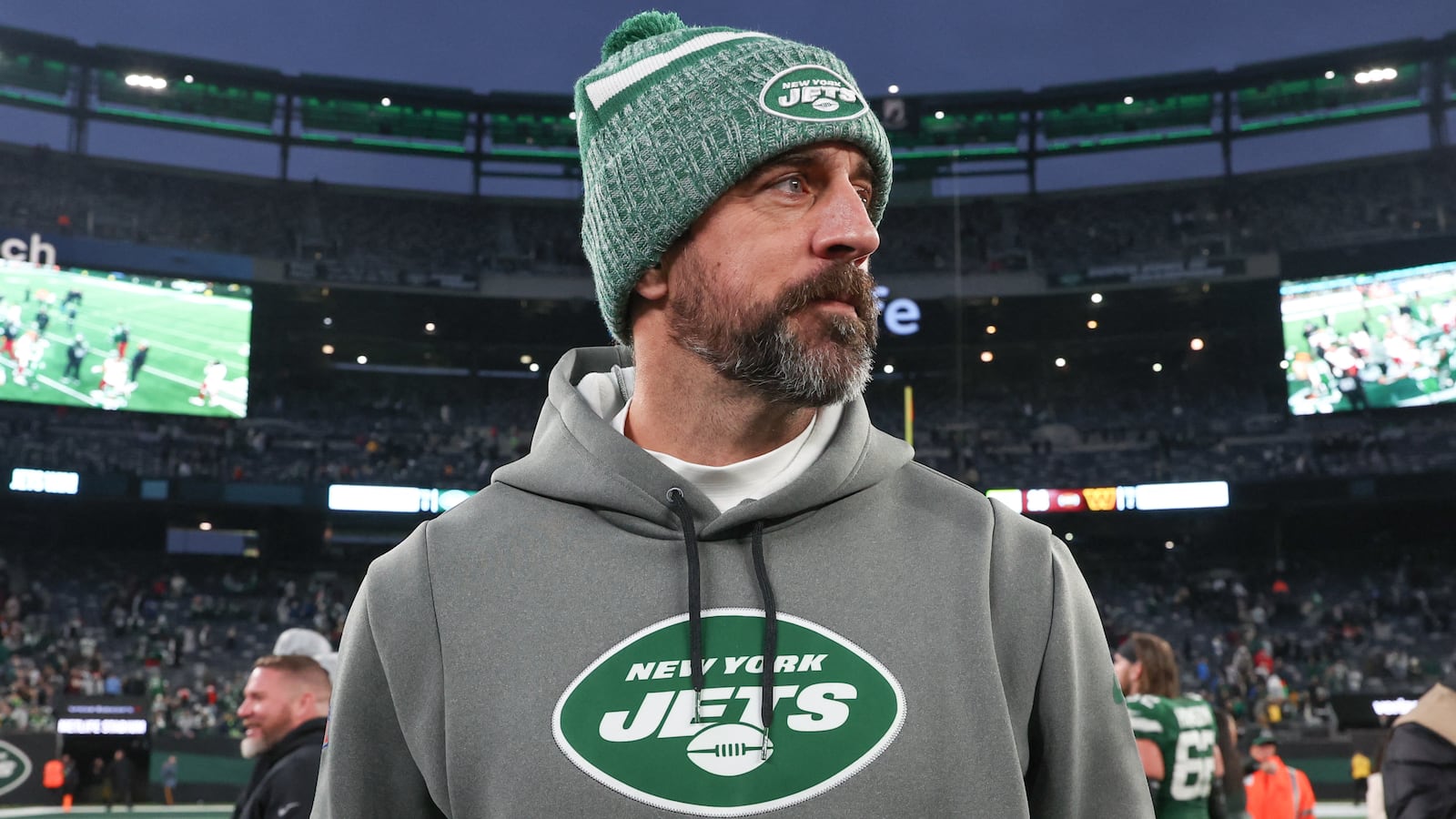 Aaron Rodgers, in New York Jets gear, walks on an NFL field.